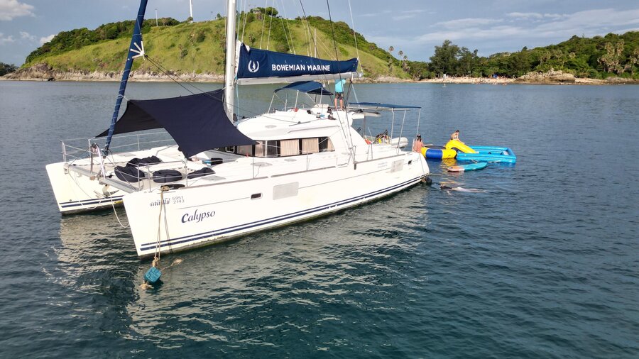 Sailing catamaran at anchor beside a green island
